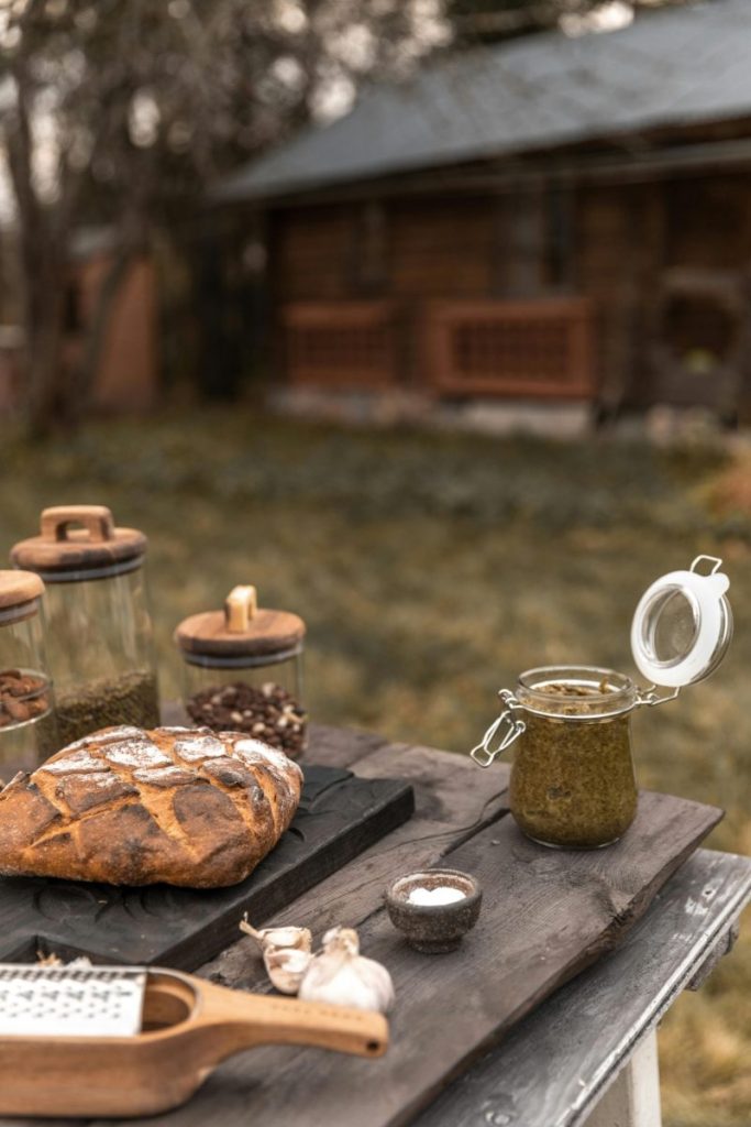 A rustic outdoor table with bread, garlic, and herbs, set in a serene backyard.